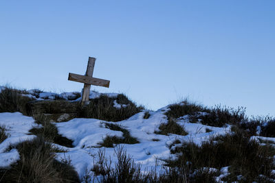 Cross on snow covered landscape against clear blue sky