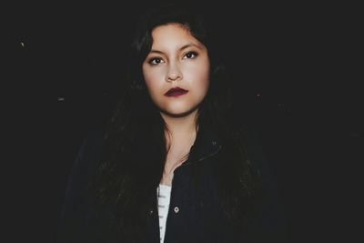 Close-up portrait of young woman standing against black background