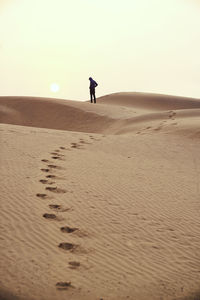 Silhouette man standing on sand in desert against clear sky