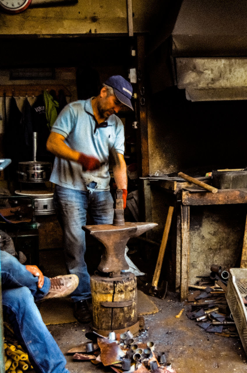 working, real people, workshop, occupation, men, one person, craft, indoors, art and craft, skill, blacksmith, holding, craftsperson, preparation, creativity, business, casual clothing, heat - temperature, metal industry