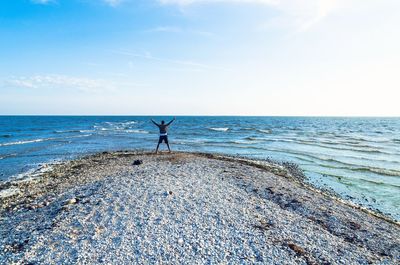 Man standing with arms raised on beach against sky