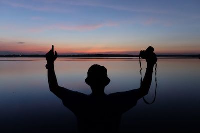 Silhouette man photographing by sea against sky during sunset