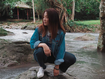 Full length of woman crouching on rock by stream