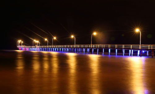 Illuminated bridge over river against sky at night