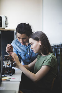 Female teacher assisting teenage student preparing robot on desk in classroom at high school