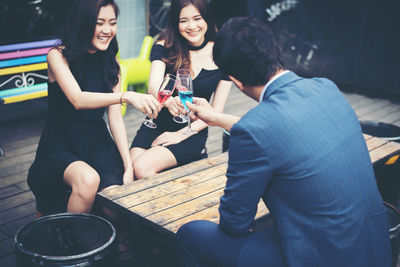 Rear view of young man with happy friends toasting drinks at bar