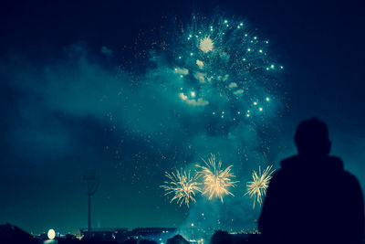 Rear view of silhouette man standing against firework display at night