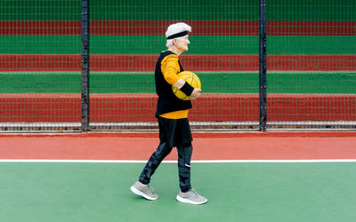 Side view mature female in activewear and headband looking away while walking with ball during basketball game