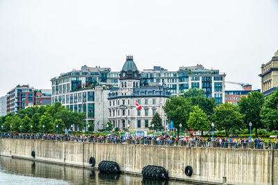 People at riverbank against clear sky in city