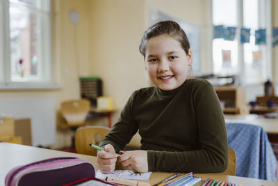 Portrait of smiling female pupil sitting at desk in classroom