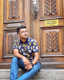 Portrait of young man sitting on wooden door