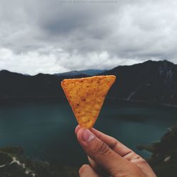 Person holding chip against lake sky