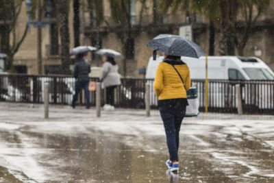 Rear view of woman with umbrella walking on wet city street during monsoon