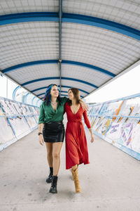 Happy women walking arm around on footbridge