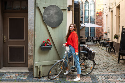 Pretty brunette with long hair in a red sweater and jeans on a vintage bike in the old town