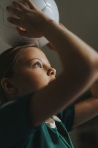 Elementary girl carrying sports ball on head at home