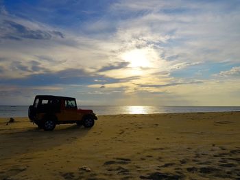 Truck on beach against sky during sunset