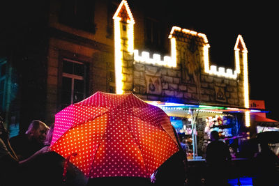 Rear view of person with red umbrella standing on street at night