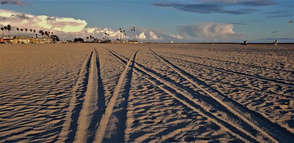 Tire tracks on sand at beach against sky