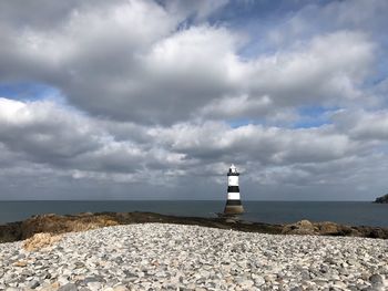 Lighthouse on rock by sea against sky