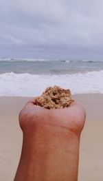 Close-up of hand on sand at beach against sky