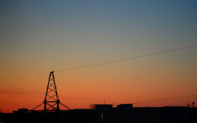 Silhouette electricity pylons against clear sky at sunset