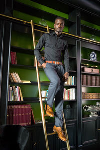 Portrait of young man standing on ladder in library