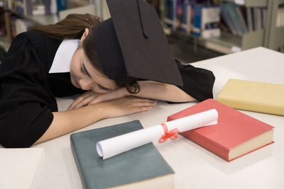 Student in graduation gown napping at table