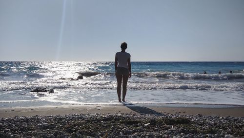 Rear view of man standing on beach against clear sky