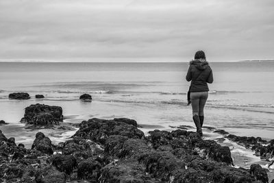 Rear view of woman standing on beach against sky