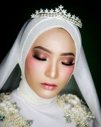 Close-up of beautiful young woman with make-up wearing tiara against black background