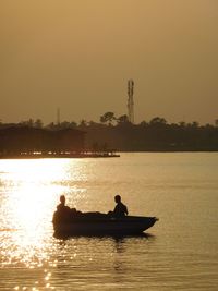 Silhouette people on boat sailing in river against sky during sunset