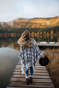 Young blonde female standing on the wooden pier near the autumn forest. travel,lifestyle concept.	