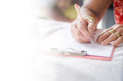 Cropped hand of woman writing in paper at table