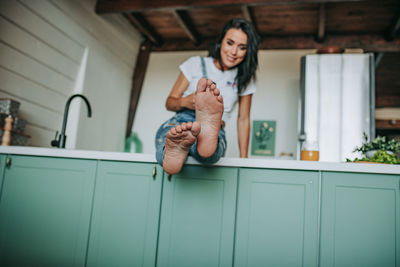 Woman drinking juice while sitting in kitchen counter