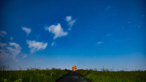 Empty road amidst grassy field against blue sky at night