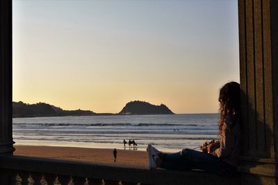 Full length of woman looking at beach while relaxing on retaining wall