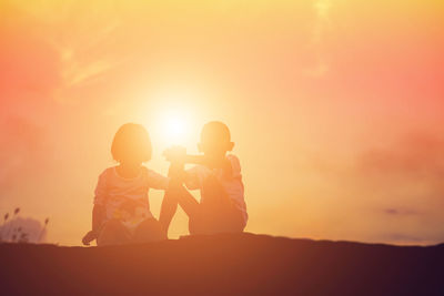 Siblings sitting on land against sky during sunset