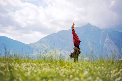 Side view of woman doing handstand on grassy field against mountains