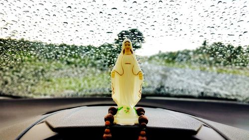 Close-up of virgin mary souvenir with praying beads on dashboard against wet windshield