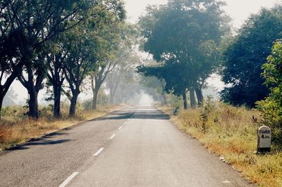 Empty road amidst trees against sky