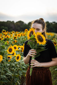 Portrait of young woman holding sunflowers while standing at farm