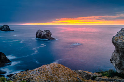 Rocks in sea against sky during sunset