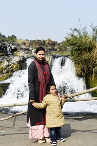 A young woman with her daughter standing near to a waterfall