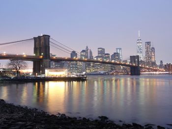 Illuminated bridge over river by buildings against sky