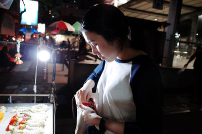 Side view of young woman buying at market stall during night