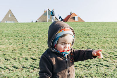 Close-up of girl pointing while standing in warm clothing on grassy field