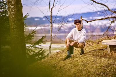 Young man crouching on field at forest