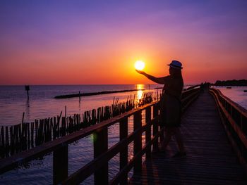 Man standing on pier over sea against sky during sunset
