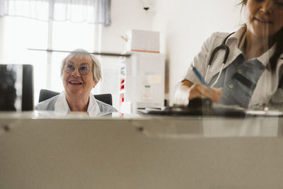 Female doctor writing prescription by senior nurse looking away